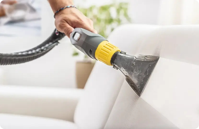 Individual cleaning a couch with a vacuum cleaner