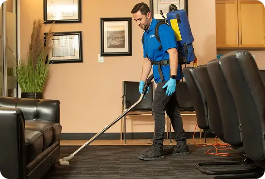 A man in a blue shirt and gloves is actively cleaning a room